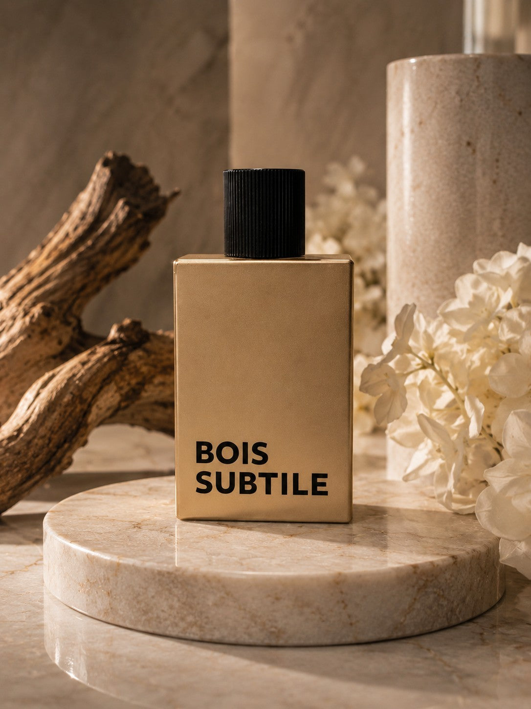 Flacon de parfum My Store Bois Subtile doré minimaliste posé sur un socle en marbre avec du bois flotté et des fleurs