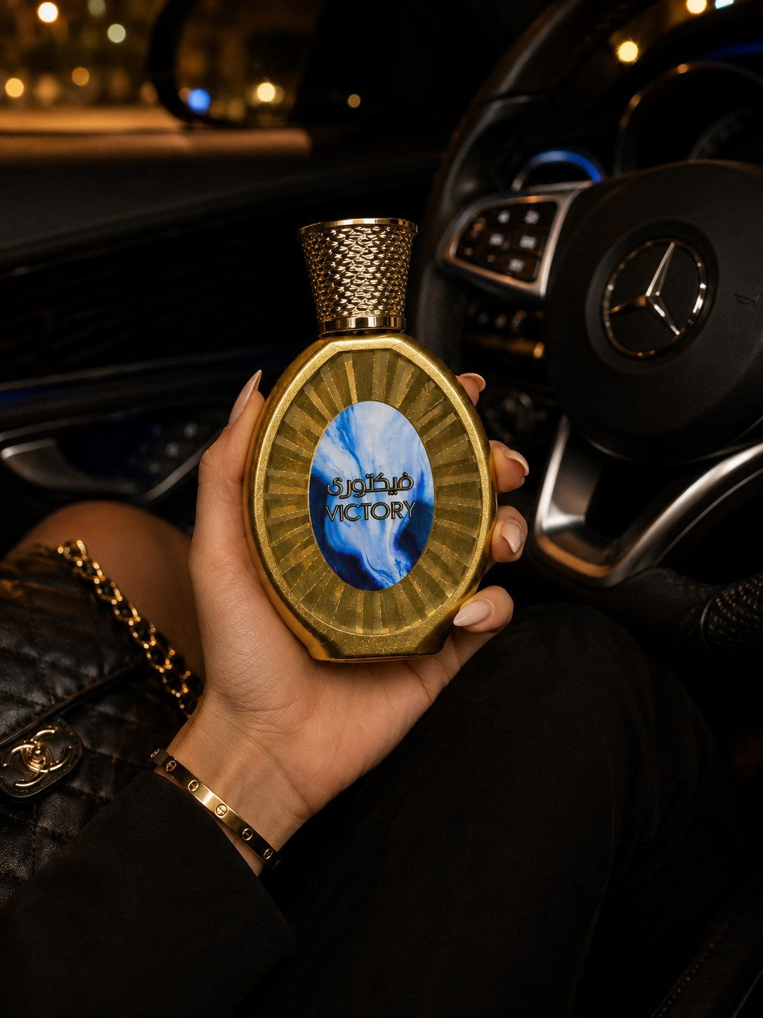 Flacon de parfum My Store Victory doré avec médaillon bleu tenu en main dans une voiture de luxe
