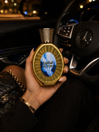Flacon de parfum My Store Victory doré avec médaillon bleu tenu en main dans une voiture de luxe